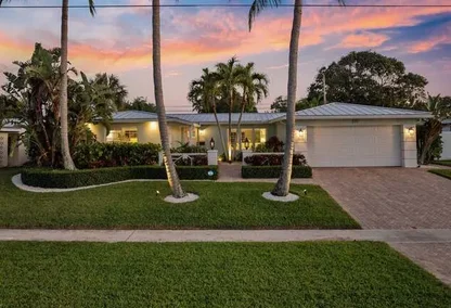 Front view of a single-story home in Chatham Hills Boca Raton with tropical landscaping, palm trees, and a sunset sky.